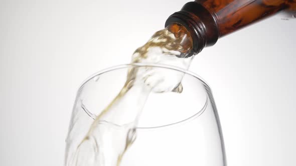 Beer is pouring with bubbles and foam in large beer glass from bottle on white background close up. alt