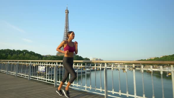 A woman running across a bridge with the Eiffel Tower alt