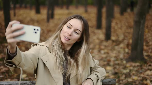 Happy Woman Sitting on the Bench in the Park and Taking a Self Portrait alt
