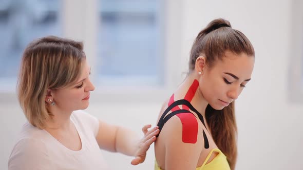 Physical therapist placing kinesio tape on woman patient's shoulder and neck alt