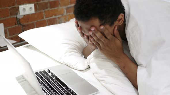 Financial Loss for African Man Working on Laptop, Lying on Stomach alt
