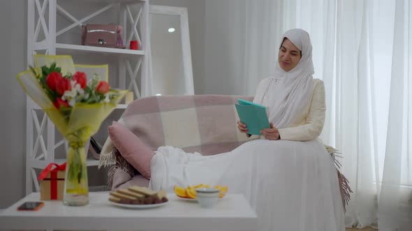 Wide Shot of Happy Smiling Middle Eastern Bride in White Wedding Dress and Hijab Messaging Online on alt