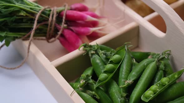 Fresh Vegetables in a Wooden Basket Green Peas Radishes Potatoes and Carrots Closeup on a White