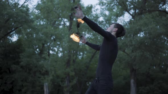 Young Man in Black Clothes Performing a Show with Flame Standing on Riverbank alt