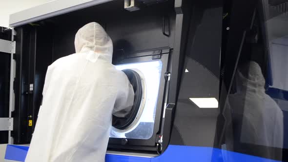 A Man in a White Protective Suit Stands Near a Large 3D Printer alt