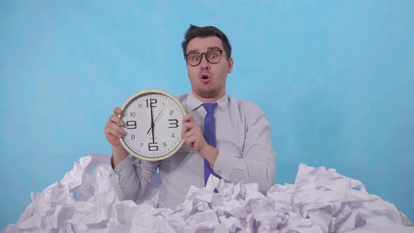 Confused Man Office Worker with a Watch Leans Out of a Large Heaps of Crumpled Paper alt
