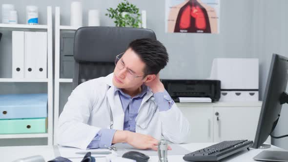 Stressed and overworked Asian male doctor sitting on table in hospital. alt
