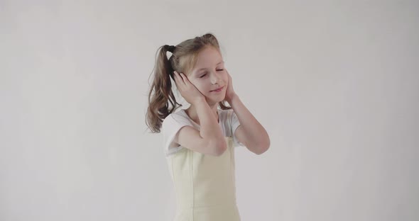 A young girl with two ponytails simulating listening to music with headphones.