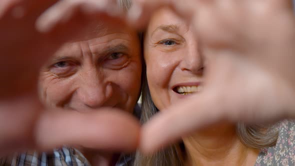 Close Up of Senior Beautiful Couple Doing Heart Shape with Hands at Home alt