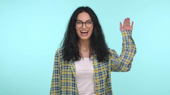 Attractive Young Woman with Long Curly Hair Wearing Glasses Waving Hand and Saying Hi Greeting