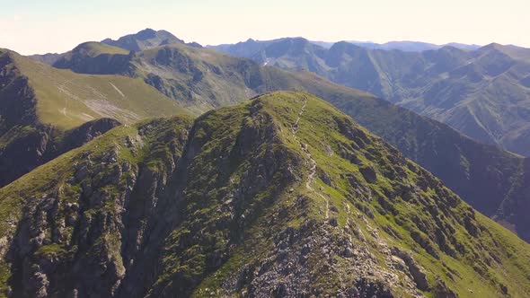 Ascending aerial view of green mountain peak and narrow trail leading to summit. View from drone of alt