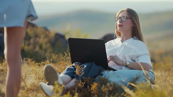 Female Freelancer is Sitting on Bag Chair in Fresh Air Working on Laptop and Explaining Her Idea for alt