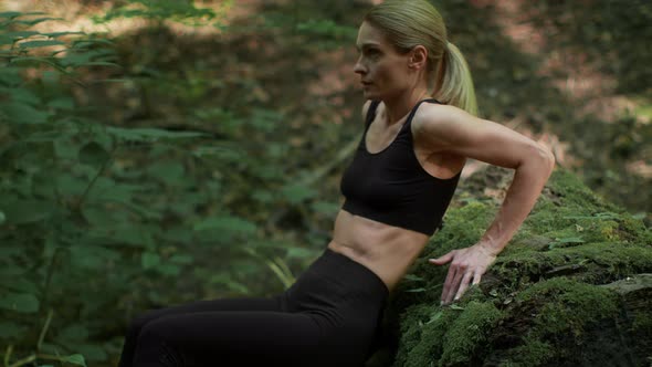 Middle Aged Woman Exercising at Woodland Practicing Reverse Pushups Leaning at Mossy Stone Tracking alt