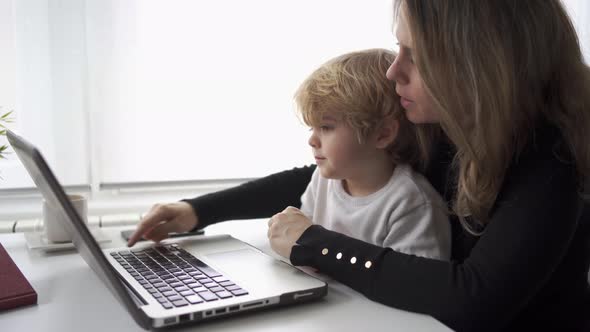Woman with little kid working on laptop at home alt