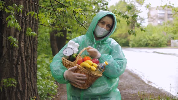 A Female Volunteer Delivers Food During the Coronavirus Pandemic in Cloudy Weather in a Raincoat