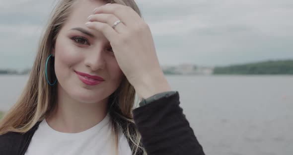 Happy Girl Corrects Her Blowing Hair and Smiles at Camera at Seaside Nature alt