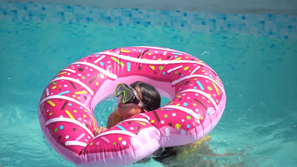 Cute Little Girl in a Bathing Suit Lying on a Donut Inflatable Circle