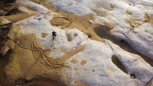 Aerial: Dirtbiker Extreme Ride Driving on Paved Stone with Sand in the River. alt
