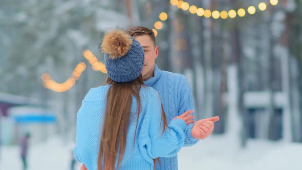 Young Man Hugs Girlfriend in Blue Sweater on Ice Rink
