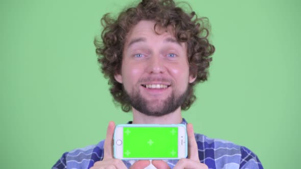 Face of Happy Young Bearded Hipster Man Showing Phone alt