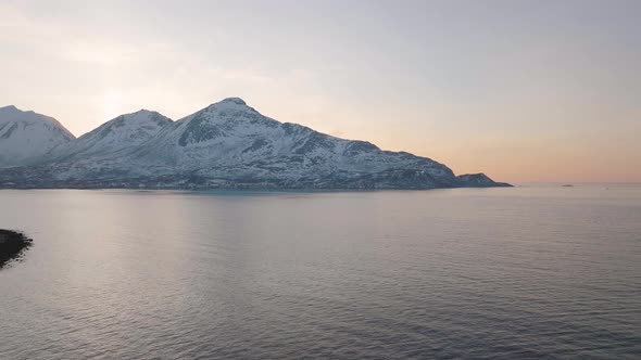 Snowy mountains in inhospitable arctic circle, orange glow at sunset; drone alt