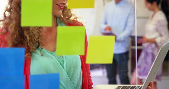 Female executive looking at sticky notes while using laptop alt
