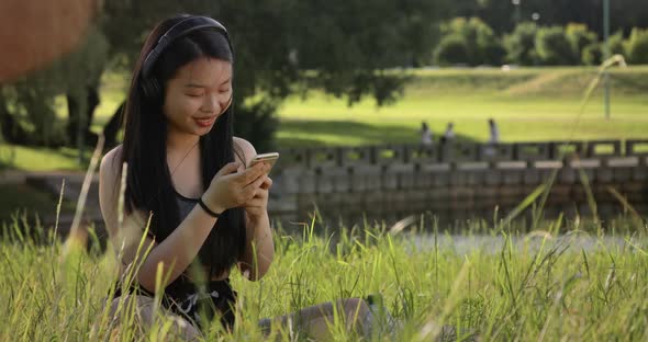 Slow Motion of Asian Young Woman Using Headphones for Listen to Music in Park with Use Mobile Phone