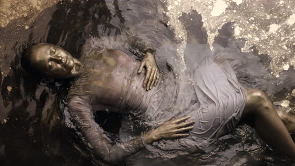 Young Graceful Woman Is Lying on Shallow with Colored Gold Water Face Is Covered Golden Dye alt