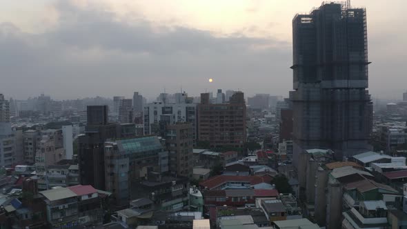 Forwarding movement of a Drone shot of Taipei during sunset. The sun is hiding behind a large cloud alt