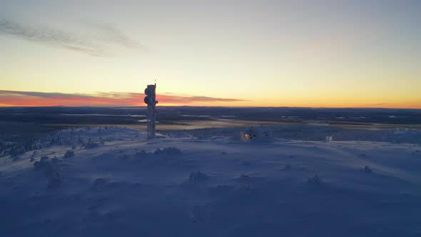Aerial view rising above sunrise remote Nordic Lapland cabin and communications tower in polar snow alt