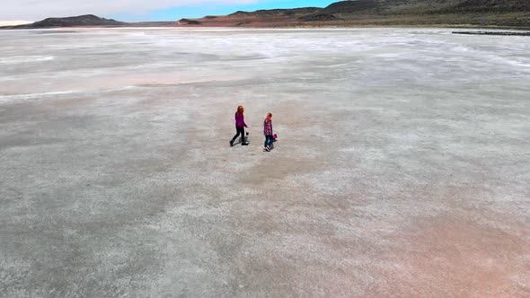 Aerial low level rotating pan of a Mother, daughter and dog walking on a desolate landscape by the g alt