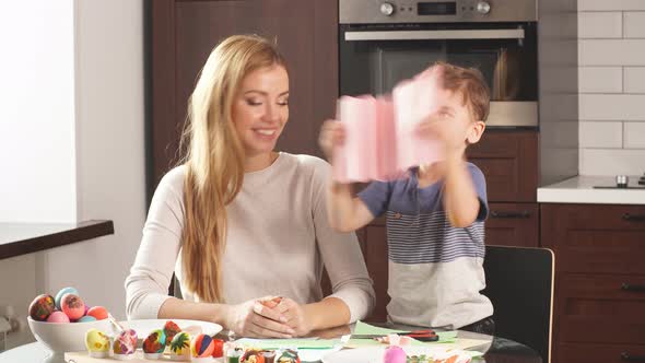Woman and Little Boy with Smiling Faces Making Decorations. Mother and Son Painting Eggs for Easter alt