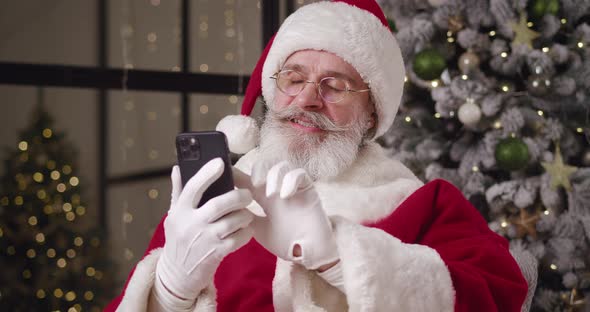 Cheerful Kind Santa Claus Browsing Websites Swiping Surfing on Internet Using Smartphones and alt