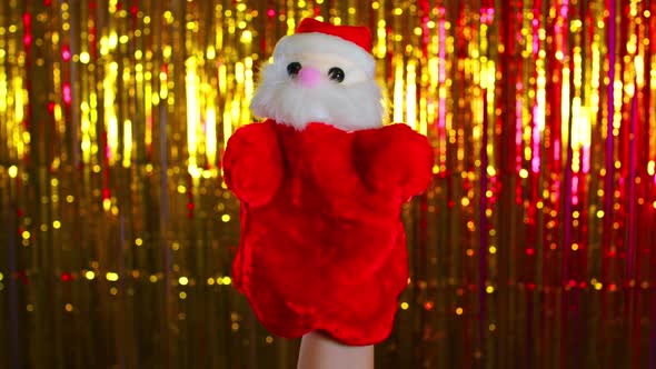 Person Showing Santa Claus Toy Against Golden Christmas Tinsel alt