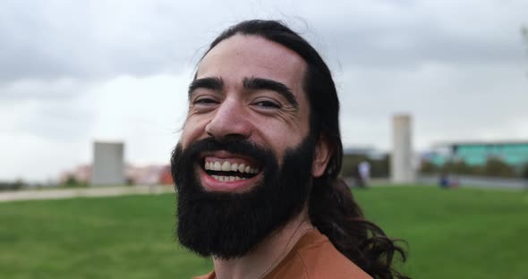 Happy hipster man with long hair laughing on camera at city park alt