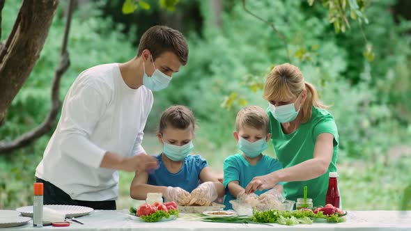 Dad and mom teach children how to cook grilled meat, Family in medical masks on a picnic in nature