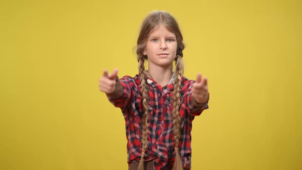 Slim Teenage Caucasian Girl Pointing Forefingers Looking at Camera Posing at Yellow Background alt