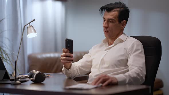 Tired Middle Eastern Businessman Sitting in Home Office Checking Smartphone and Stretching alt