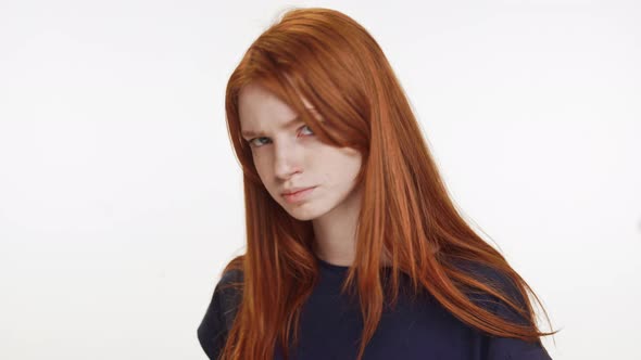 Outraged Redhaired Caucasian Teenage Girl Standing on White Background Looking at Camera and Away alt