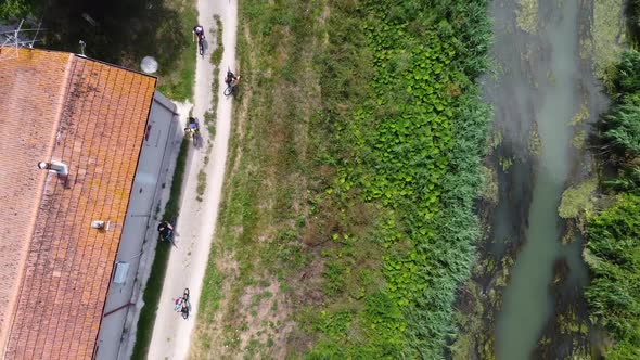 Aerial top down shot of a group of cyclists arriving at a house in front of a river alt