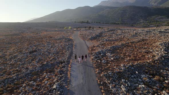 Four young tourists walking along empty rocky rural road in the countryside alt