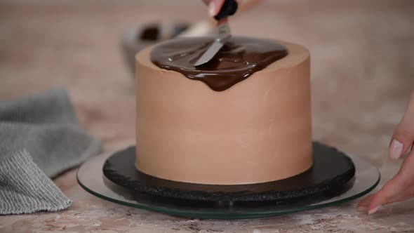 Pastry chef is smearing liquid chocolate glaze on cake with knife to decorate it. 