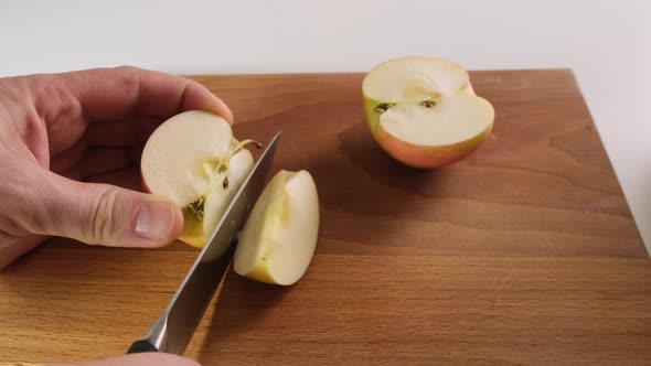 Person cuts a red Apple with knife on a wooden Board. Close up