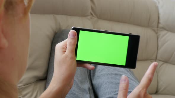 Woman relaxing and  scrolling pages on greenscreen smart phone display 4K 2160p UltraHD footage - Fe alt