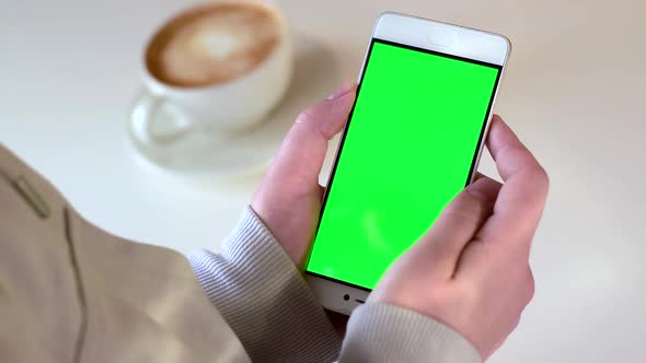 Hand Holding Green Screen Phone with a Cup of Coffee on White Table alt