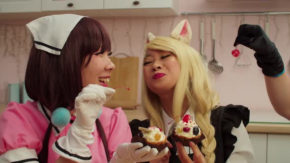 Joyful Asian Woman in Cosplay Costume Feeding Cherry Candy to Girlfriend alt