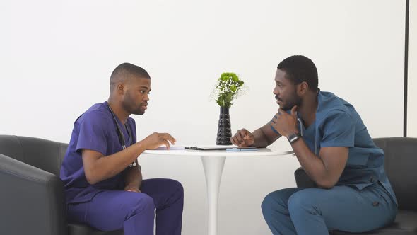 Two African American Male Colleagues Doctors Working Together Discussing and Looking at Clipboard on