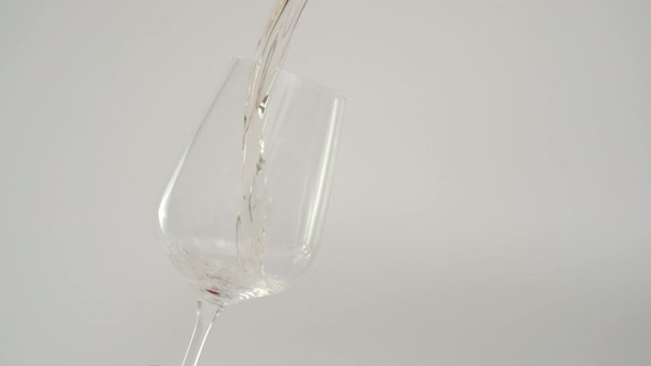 Slow Motion of Pouring White Wine in Tilted Glass White Background alt