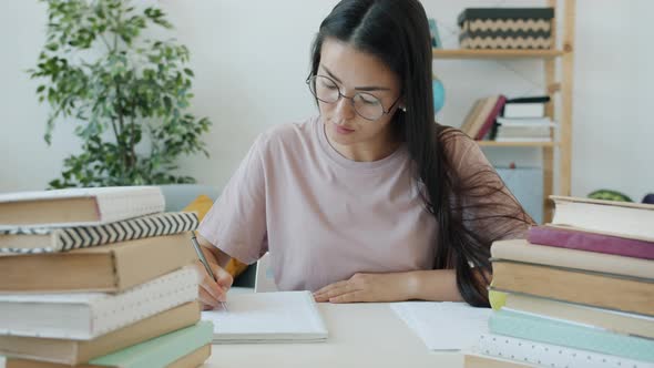 Slow Motion of Diligent Student Writing Essay Sitting at Desk with Books at Home alt
