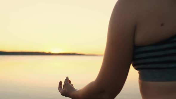 Closeup of a Girl Meditating in the Lotus Position on the Lake at Sunset
